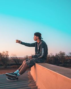 Side view of young man skateboarding against clear blue sky