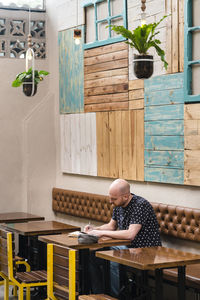 Mid adult man writing in notebook while sitting at coffee shop