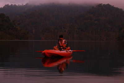 Man sitting in boat on lake against trees