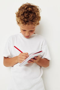 Boy writing in book against wall