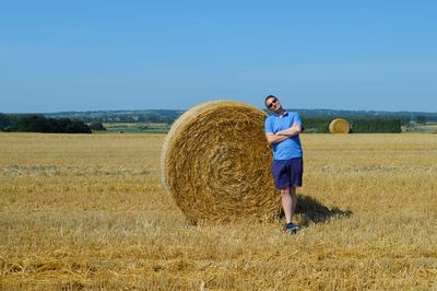 Portrait of man standing by hay bale on land against clear sky