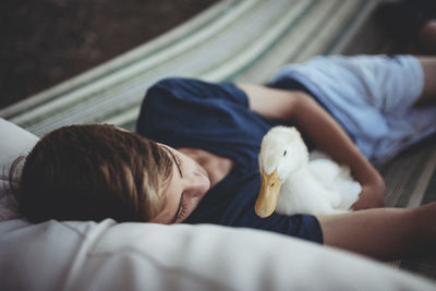 High angle view of teenage boy with duck relaxing on hammock at yard