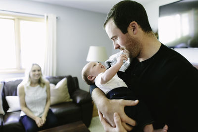 A new father holds his newborn baby son while the mom looks on