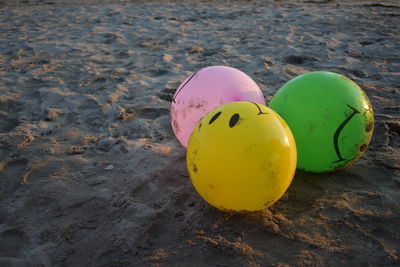 High angle view of three multi colored balloons on sand