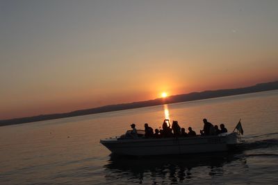 Silhouette people in sea against sky during sunset