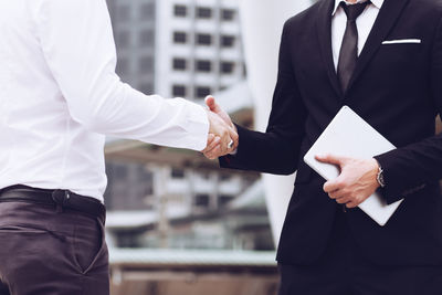 Midsection of man handshaking with colleagues in city