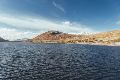 Scenic view of sea by mountain against sky