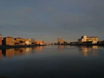 Buildings by river against sky in city