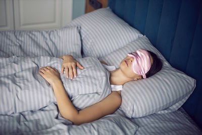 Woman in a pink eye mask lies under a blanket in a bed and suffers from insomnia