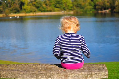 Rear view of girl sitting on bench by lake