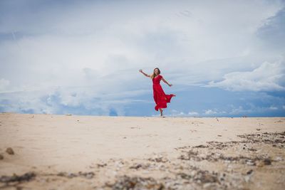 Girl playing on sand at beach against sky