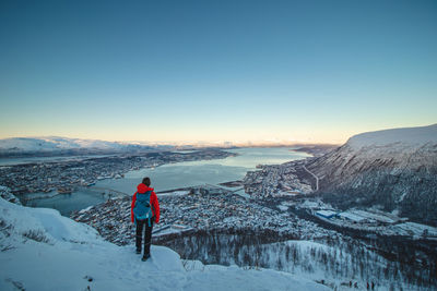 Adventurer stands atop fjellheisen and watches norwegian sea surrounding city of tromso in norway