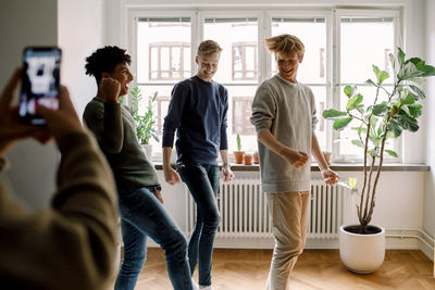 Cropped hands of girl filming teenage male friends dancing in living room