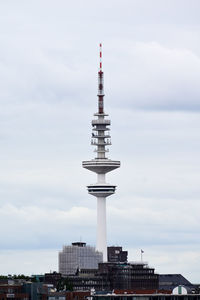 Communications tower in city against sky