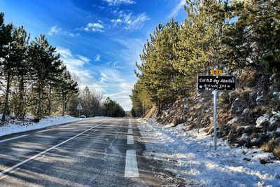 Road sign by trees against sky