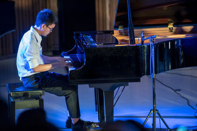 Side view of teenage boy playing piano on stage