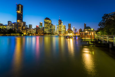 Illuminated buildings by river against sky in city at night