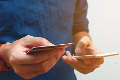 Midsection of man with credit card using smart phone against white background