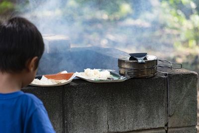 Rear view of boy standing by rice in plates on retaining wall