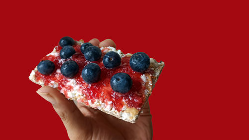 Cropped image of hand holding strawberry against red background