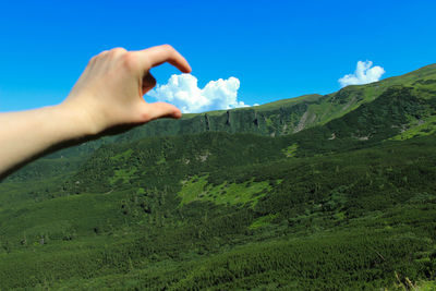 Optical illusion of person touching cloud above mountain against sky
