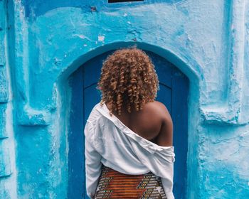 Rear view of woman standing against blue door