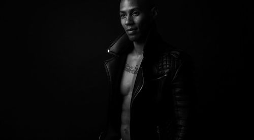 Thoughtful man wearing leather jacket standing against black background