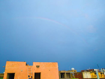 Low angle view of rainbow over buildings against blue sky