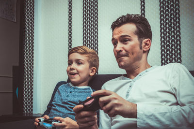 Father and son playing video game on sofa at home