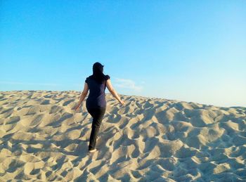 Rear view of woman walking on sand at beach against sky