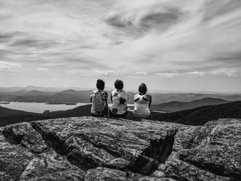 Rear view of friends sitting on mountain against sky