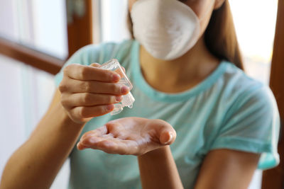 Midsection of young woman pouring sanitizer in hand at home