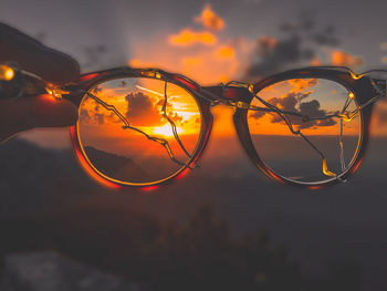 Close-up of sunglasses against sky during sunset