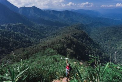 High angle view of man waving while standing on rock over mountain