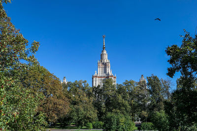 Summer silhouette of moscow university among green trees under blue sky