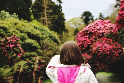 Rear view of girl with pink flowers against trees