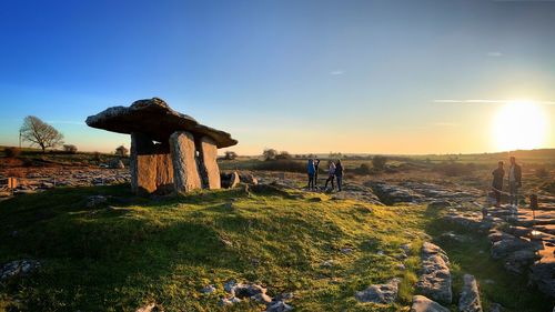 People standing by built structure on land against sky during sunset