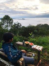 Rear view of boy sitting at market stall against sky