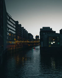 River by illuminated buildings against clear sky at dusk