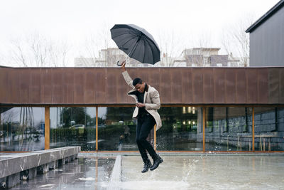 Full length of man holding mobile phone in rainy season