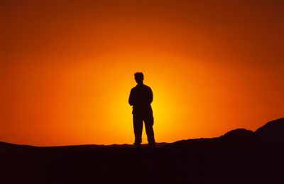 Silhouette man standing on mountain against orange sky