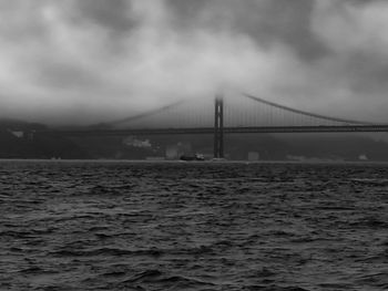 Bridge over calm sea against cloudy sky