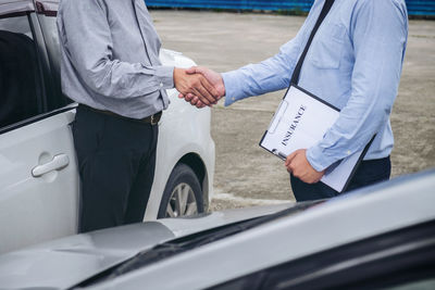 Midsection of insurance agent shaking hand with customer by car