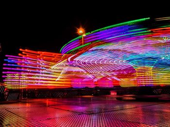 Light trails at amusement park against sky at night