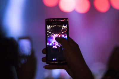 Man photographing illuminated smart phone at night