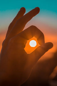 Close-up of hand holding sun during sunset