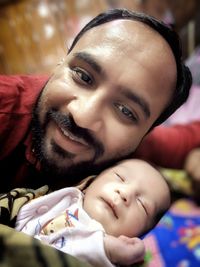 Portrait of father smiling while lying with newborn son on bed