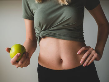 Midsection of woman holding apple while standing against gray background