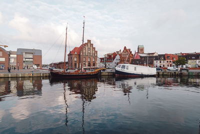 Boats moored at harbor against sky in city