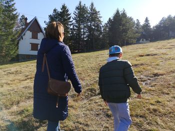 Rear view of boy walking with mother on field